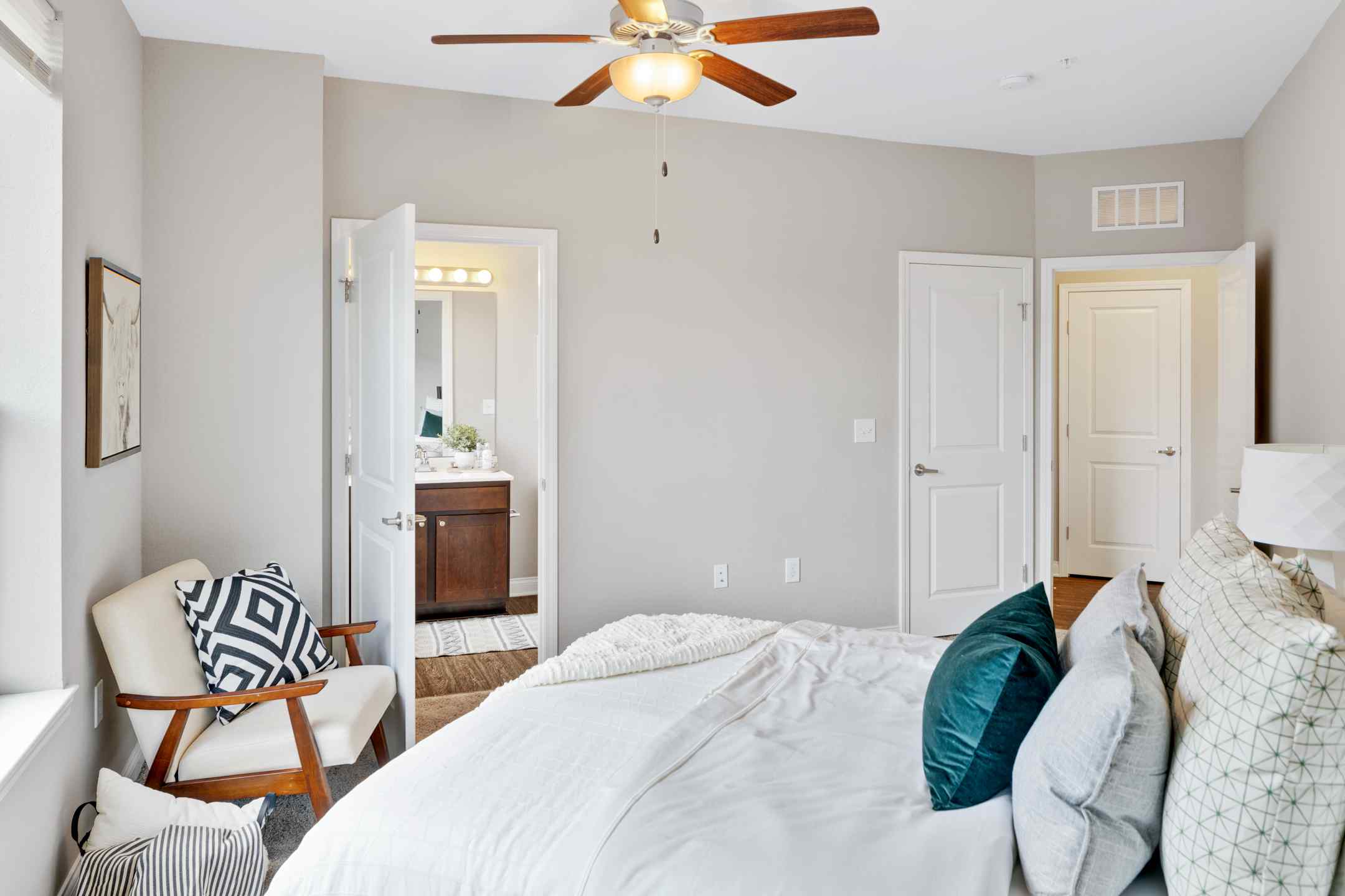 A cozy student housing bedroom with a ceiling fan and a neatly made bed, with an attached full bathroom.