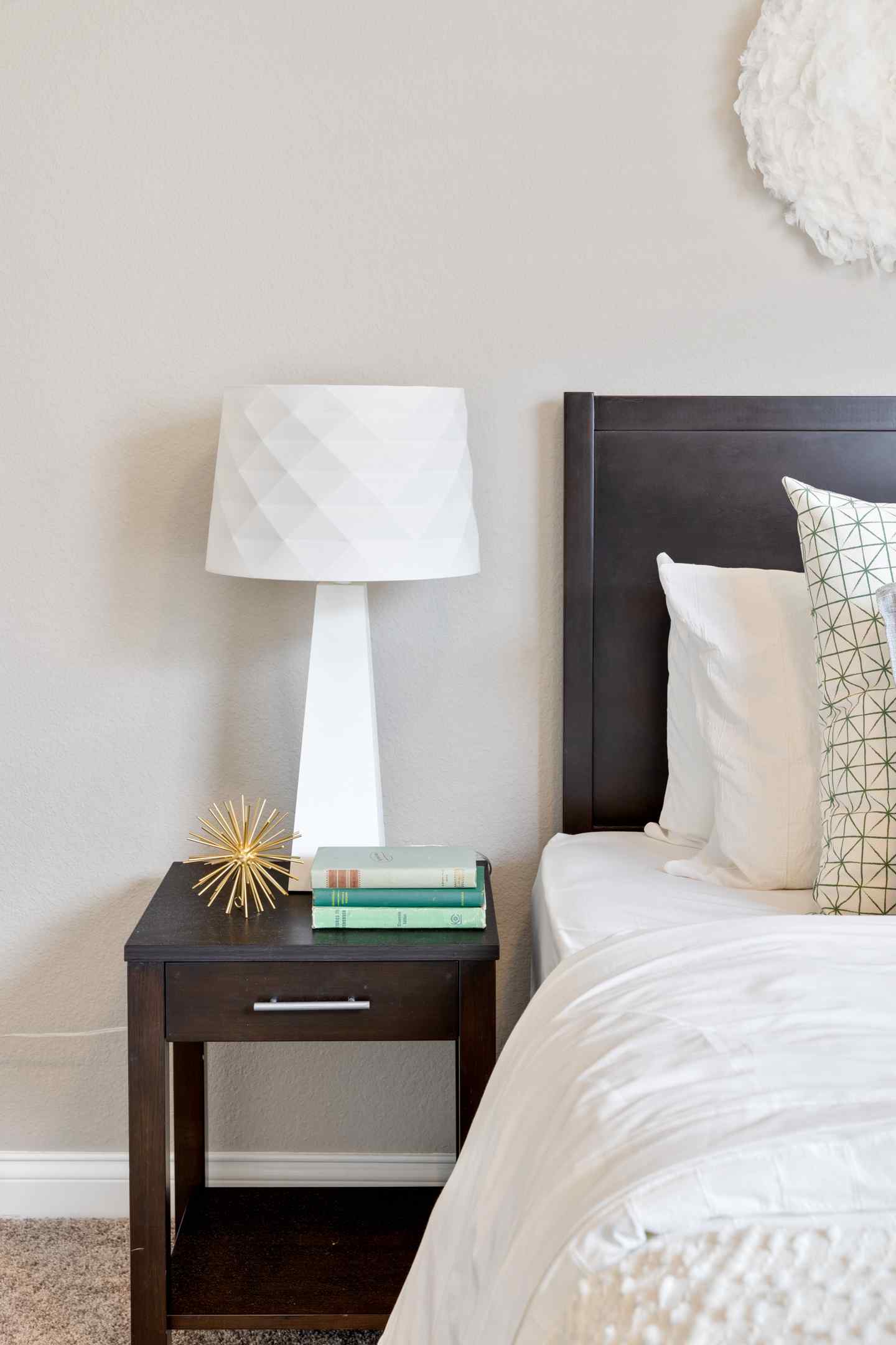 A zoomed in picture of a well decorated end table with books and a white lamp in a student's bedroom.