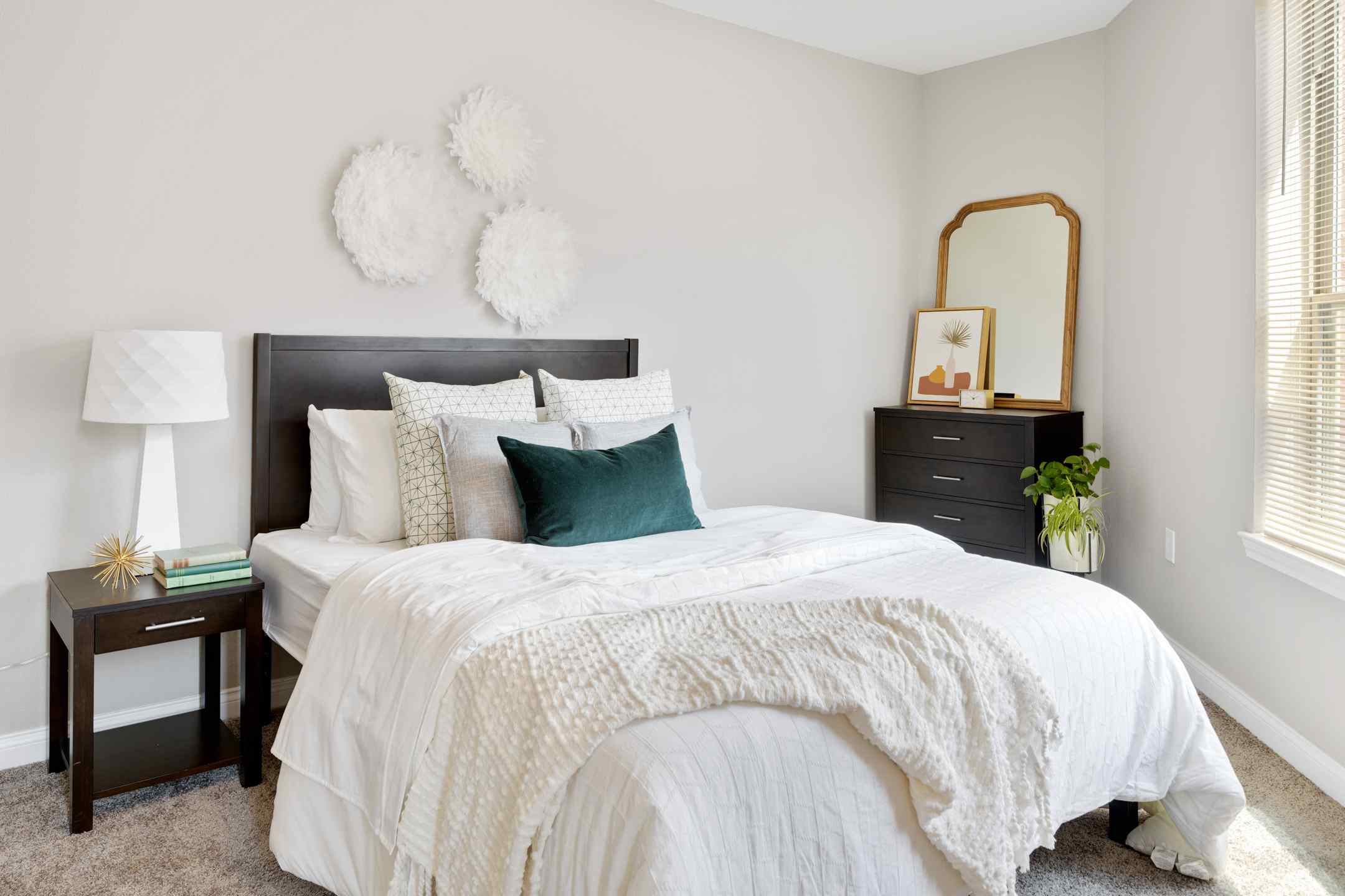 A cozy student housing bedroom with a neatly made bed and natural sunlight from a large window.